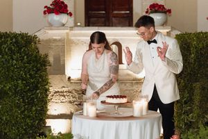 Bride and groom cutting wedding cake outdoors at candlelit ceremony with red floral decor.