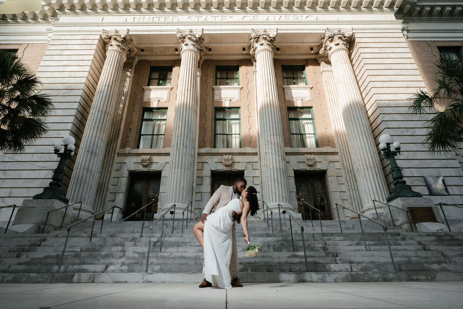 Couple sharing a romantic dip kiss on steps of grand neoclassical building with tall columns at wedding.