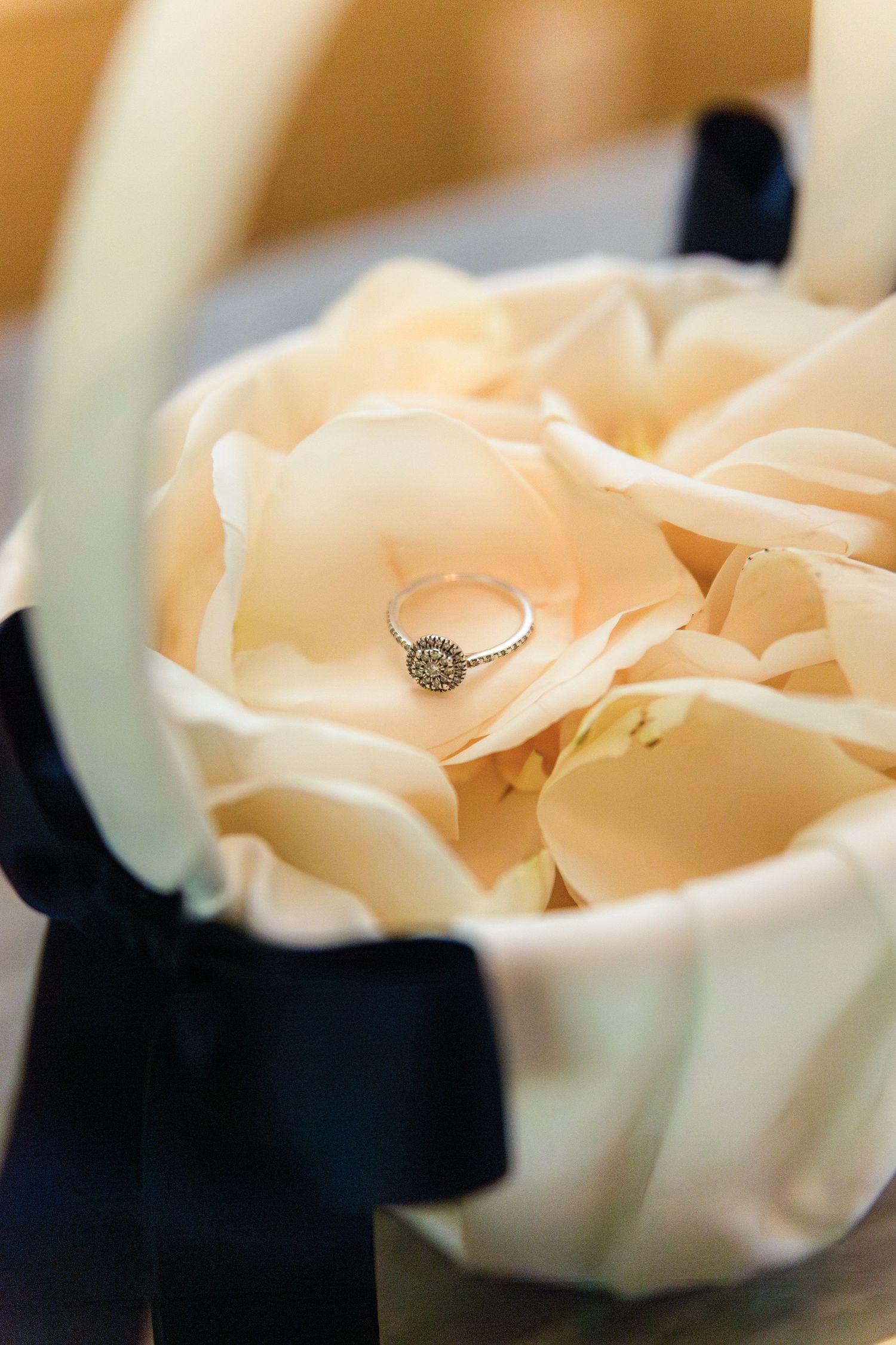 Diamond engagement ring resting in a cream satin flower basket with navy blue ribbon bow.
