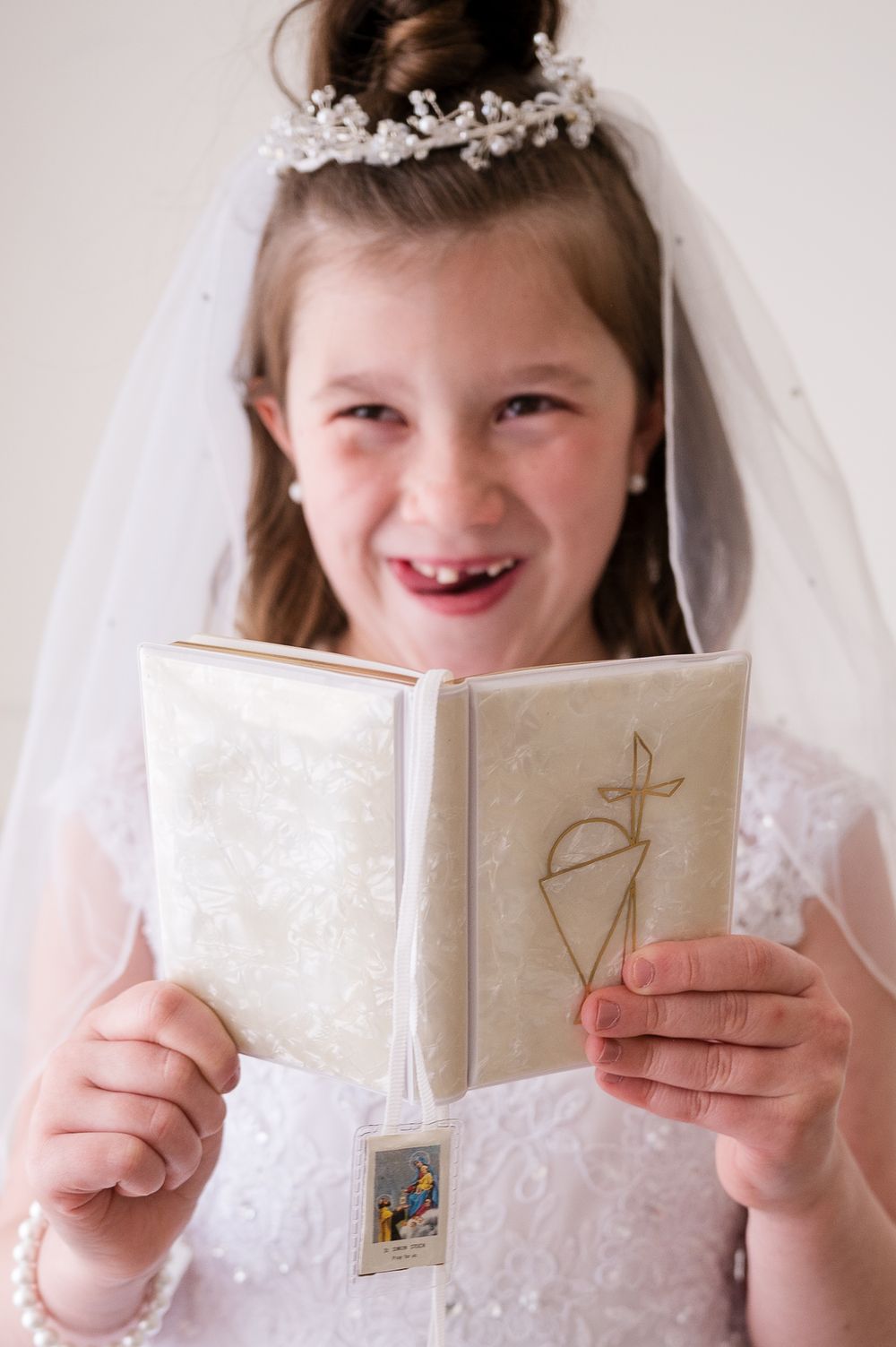 Young girl in white dress and veil holds a prayer book at her First Holy Communion ceremony.