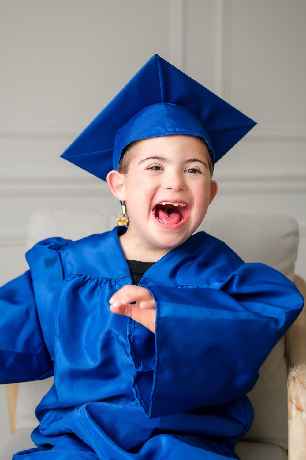 A joyful young child wearing a blue graduation cap and gown, laughing and celebrating their milestone achievement.