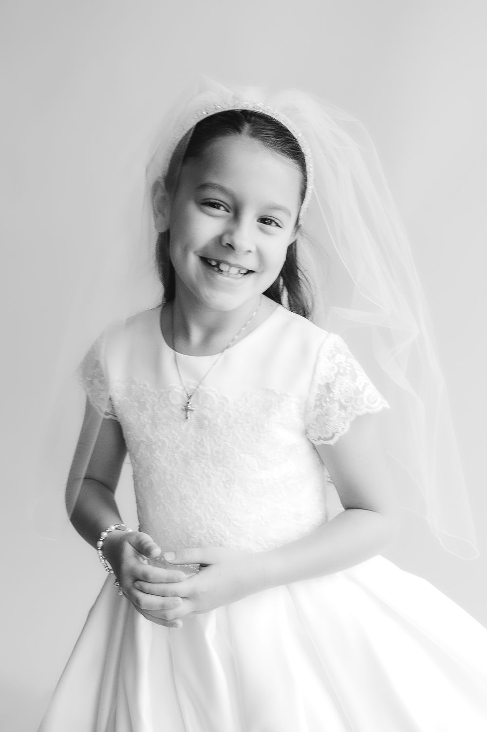 Young girl in white First Communion dress and veil smiling, black and white portrait photo.