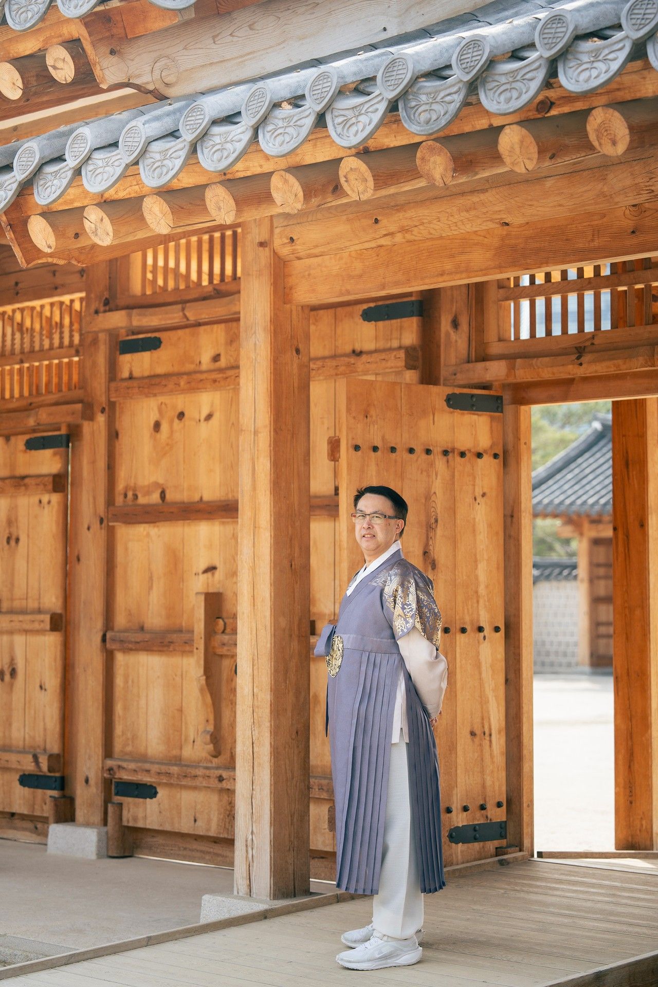 Man wearing traditional Korean hanbok standing at a wooden pavilion in a historic Korean palace.