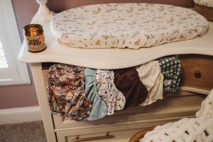 Nursery dresser with open drawer full of colorful cloth diapers and a floral changing pad.