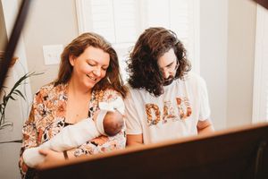 New parents admiring their newborn baby, father wearing a DAD shirt indoors.