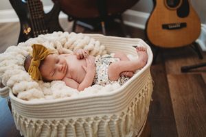 Sleeping newborn baby in woven basket with cream blanket surrounded by acoustic guitars.