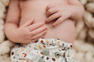 Close-up of newborn baby belly and hands wearing colorful cloth diaper.