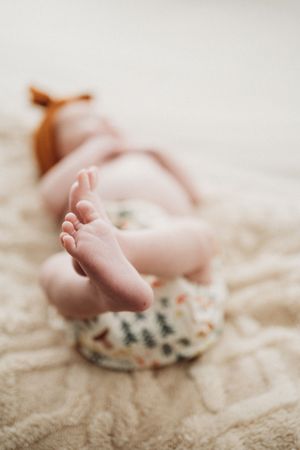 Close-up of newborn baby tiny feet in floral print pants lying on cream textured blanket.
