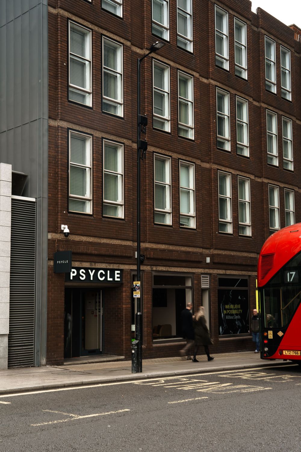 Psycle fitness studio storefront on a London street with a red double-decker bus and pedestrians passing by.