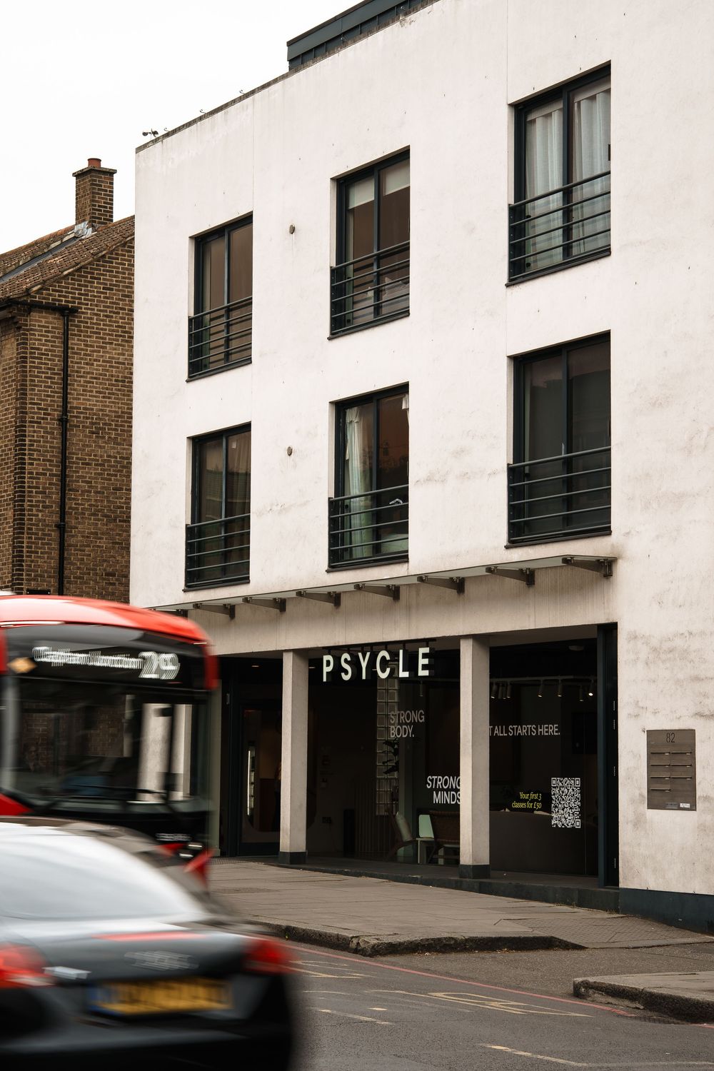 Psycle fitness studio exterior on a London street with a red double-decker bus passing by.