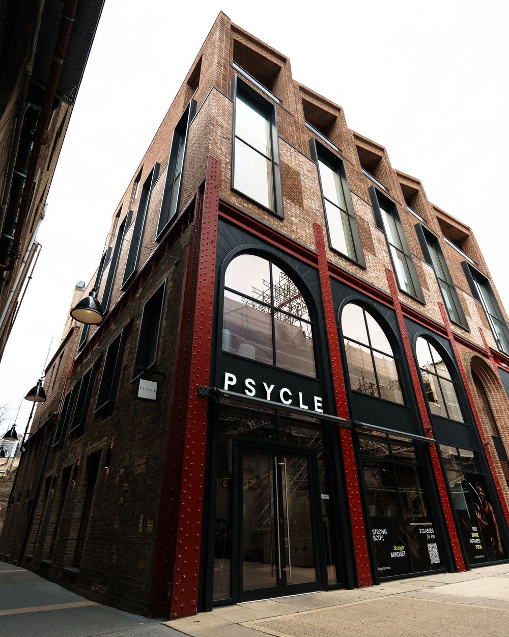 Psycle fitness studio exterior featuring red brick building with arched windows and modern signage on a city street corner.