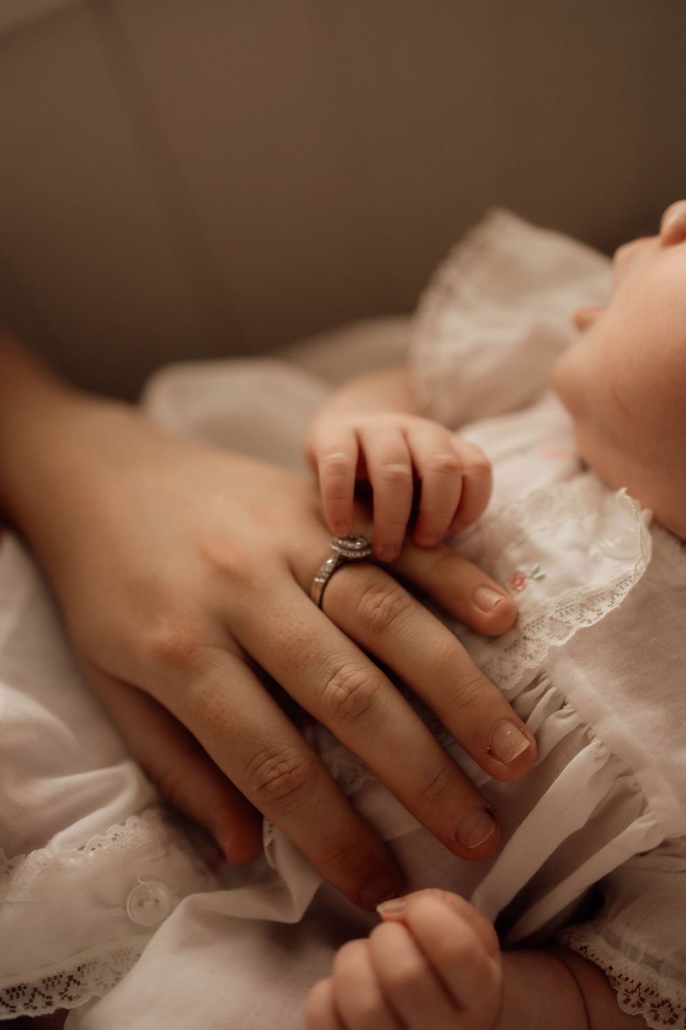 Close-up of mother wearing diamond ring gently holding newborn baby's tiny hand.