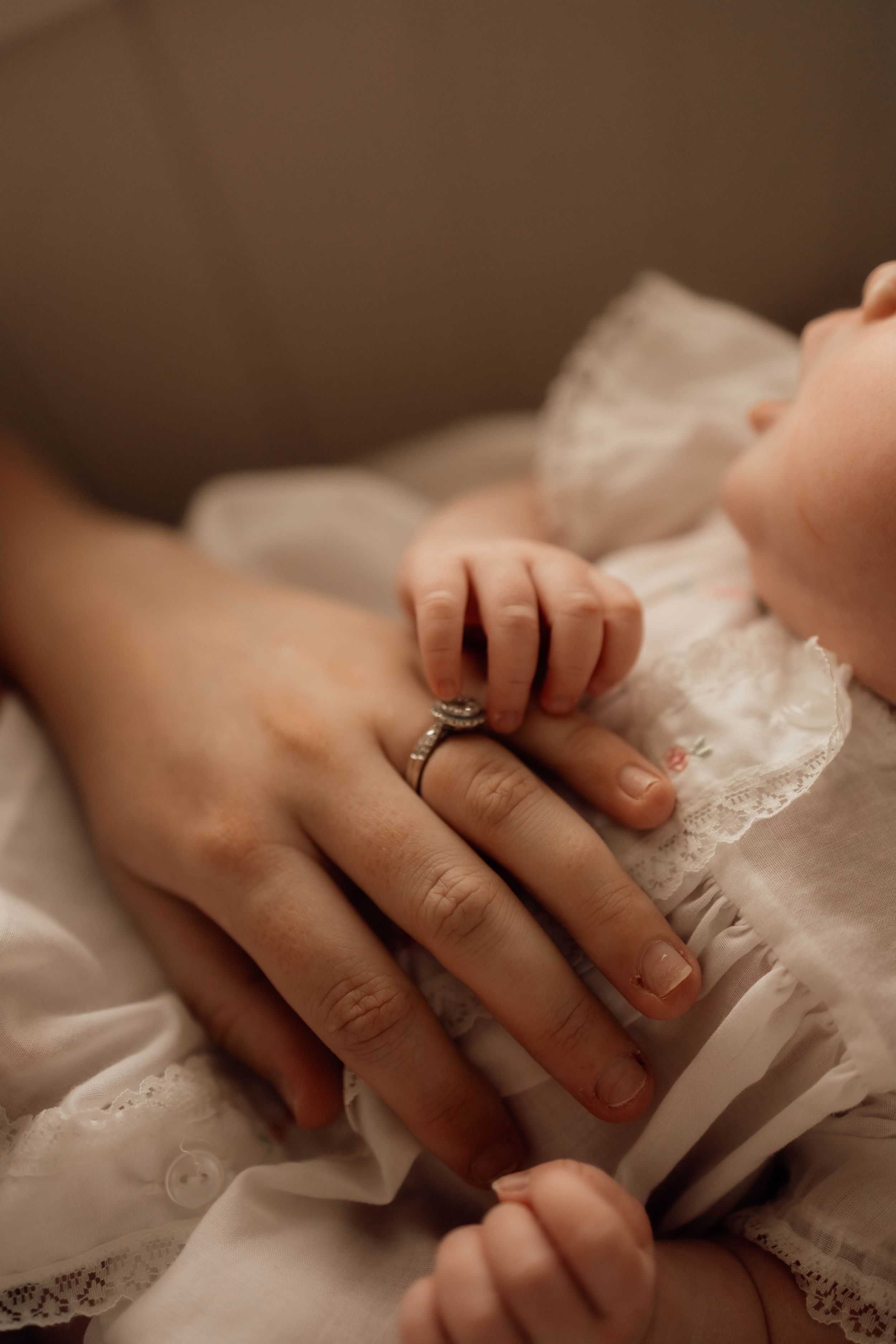 Close-up of mother wearing diamond ring gently holding newborn baby's tiny hand.