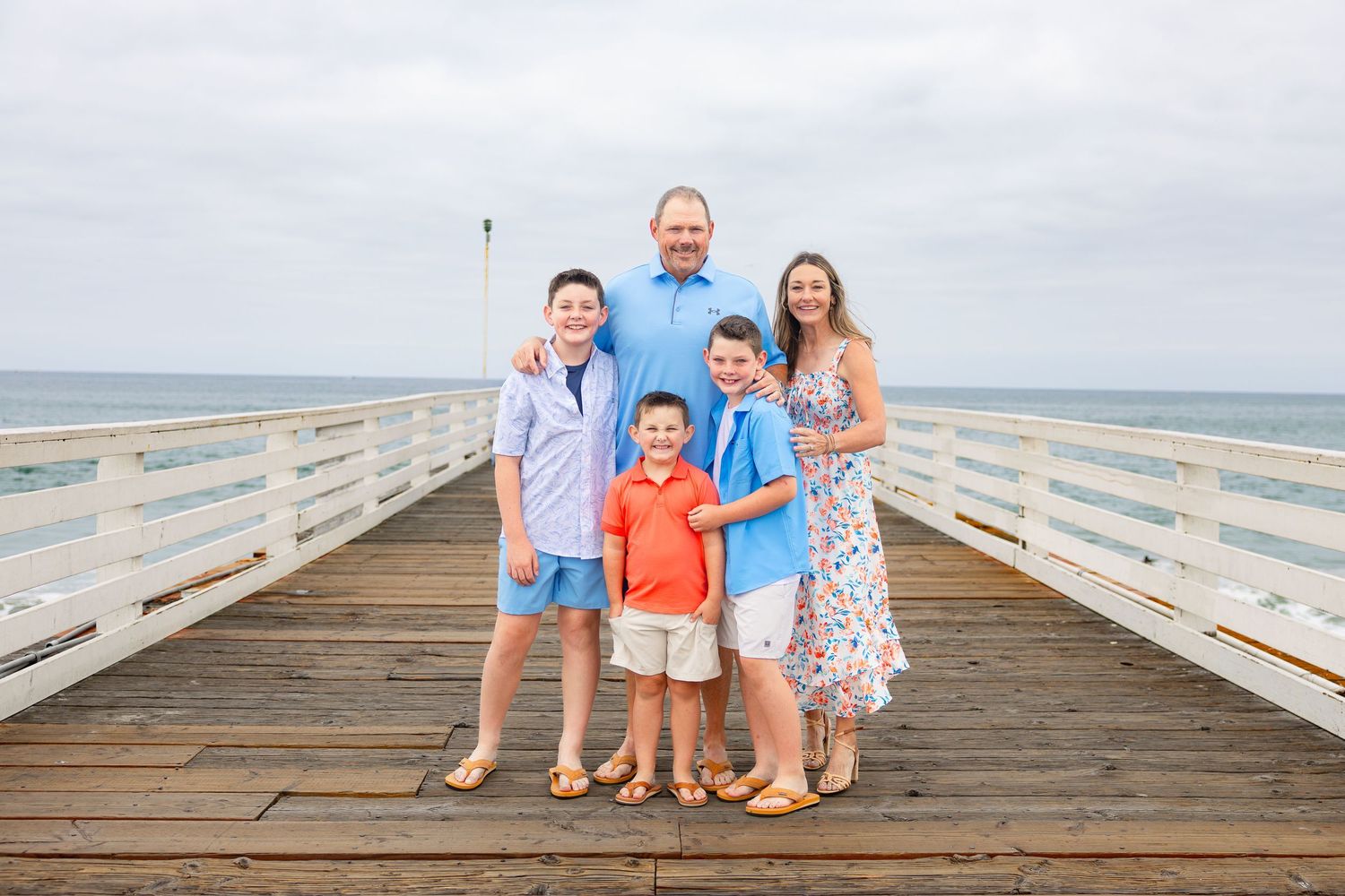 San Diego family portrait photography of a family of five posing together on Crystal Pier with the ocean in the background.