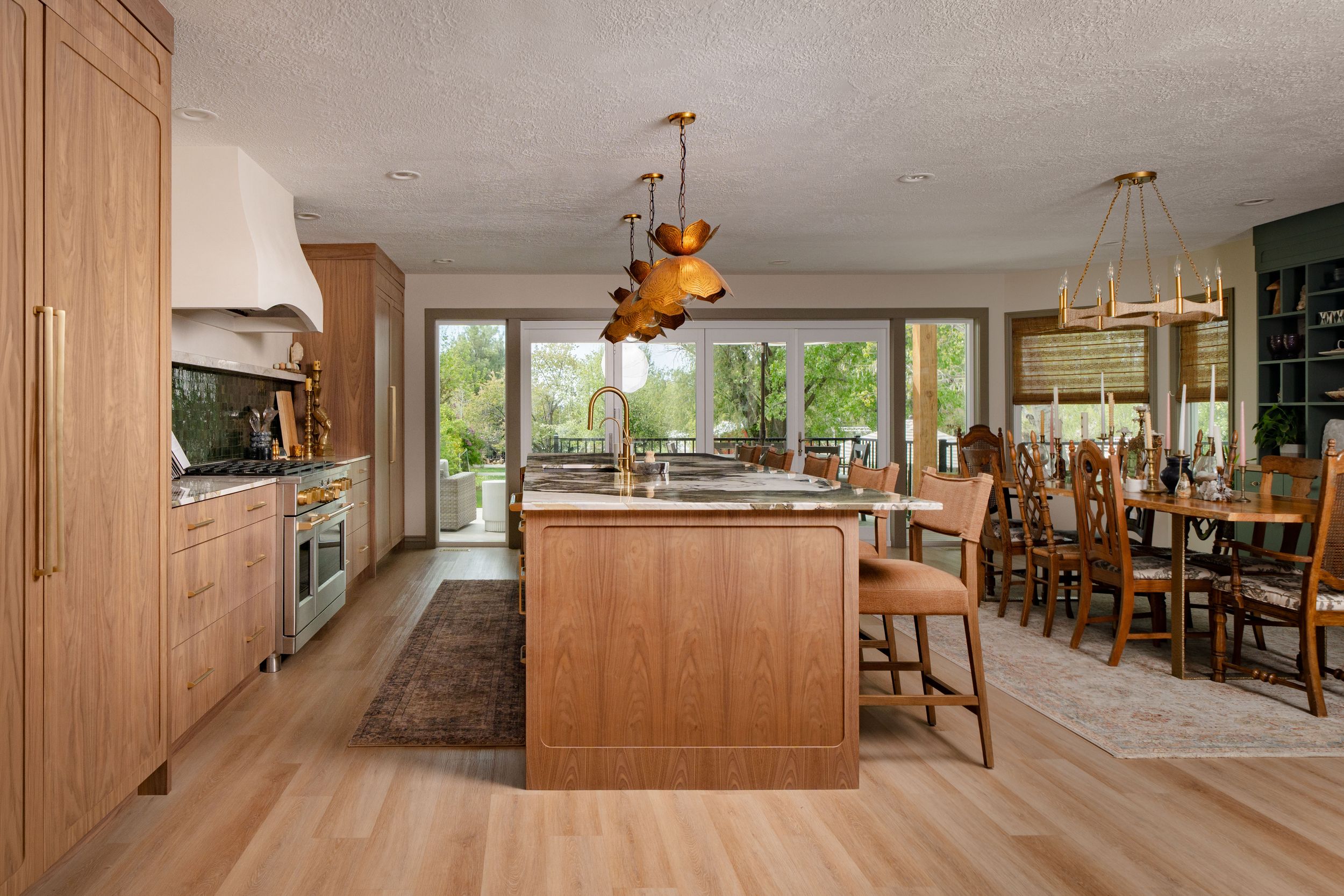 Modern kitchen with wood cabinetry, large island, pendant lights, and open dining area with natural light.