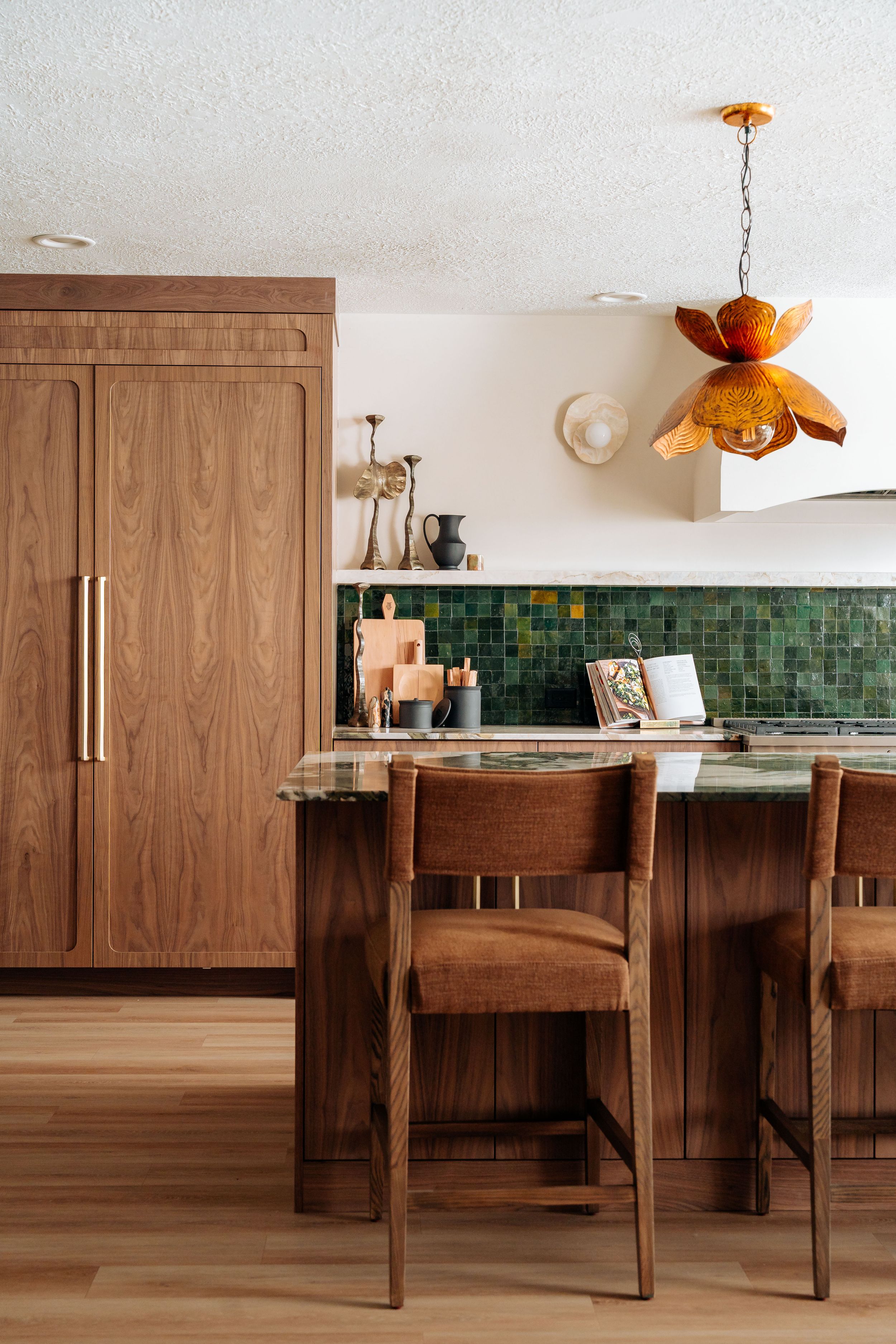 Warm mid-century modern kitchen with walnut cabinets, green tile backsplash, marble island, and an orange floral pendant light.