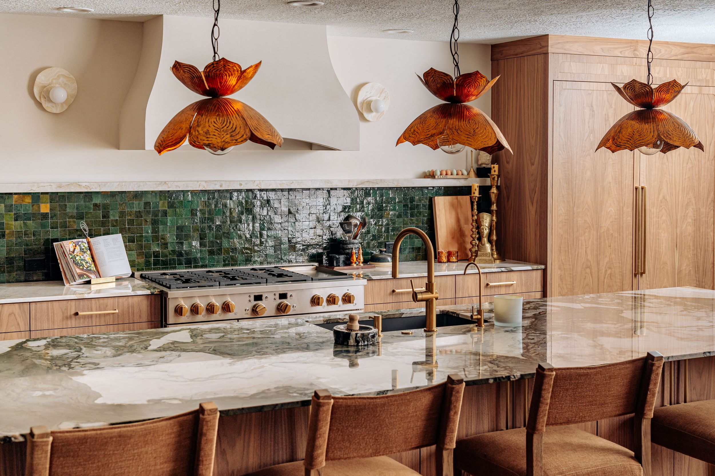 Modern kitchen with marble island, green tile backsplash, wood cabinets, and copper pendant lights.