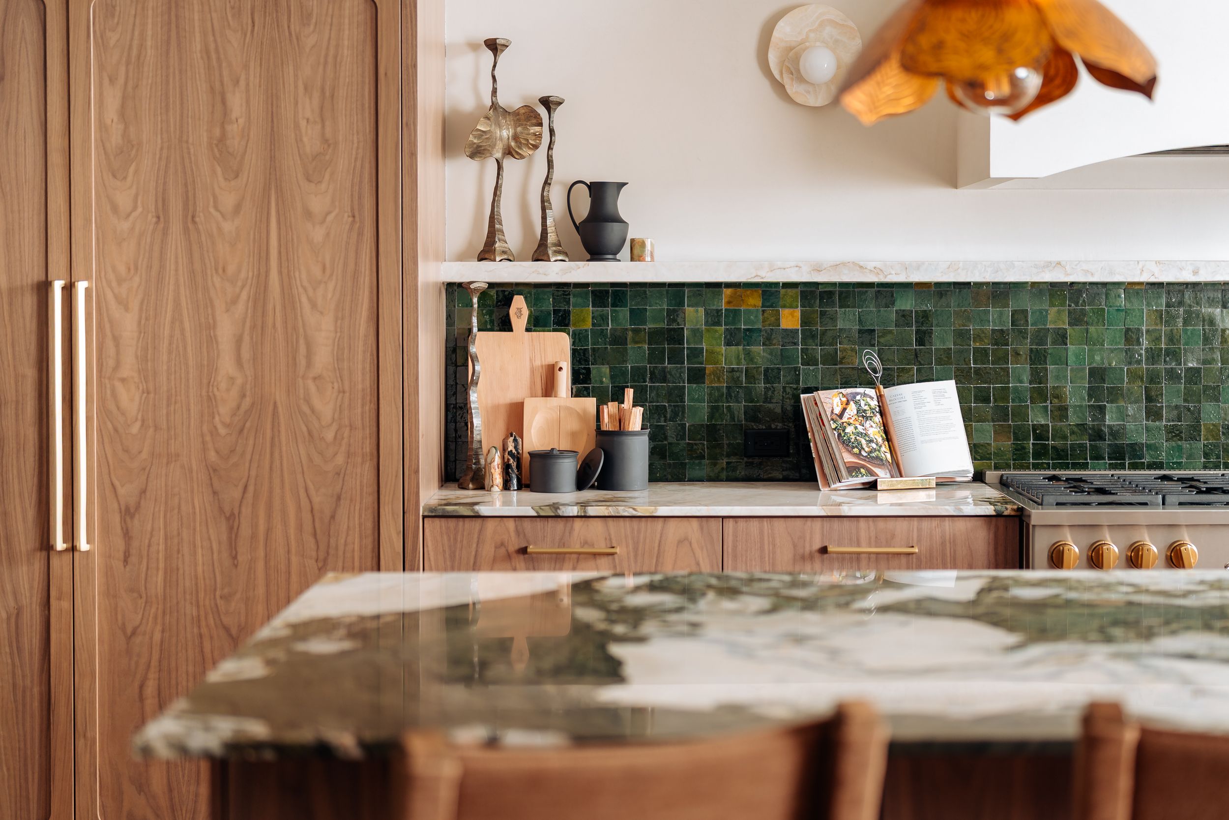 Modern kitchen with green zellige tile backsplash, walnut cabinets, brass hardware, and a green marble island countertop.