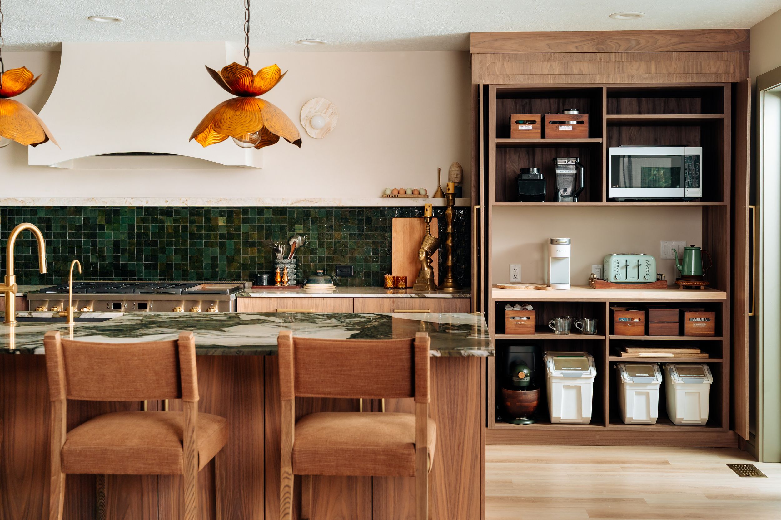 Modern kitchen with green tile backsplash, walnut cabinetry, open shelving, pendant lights, and bar stools at a stone island.