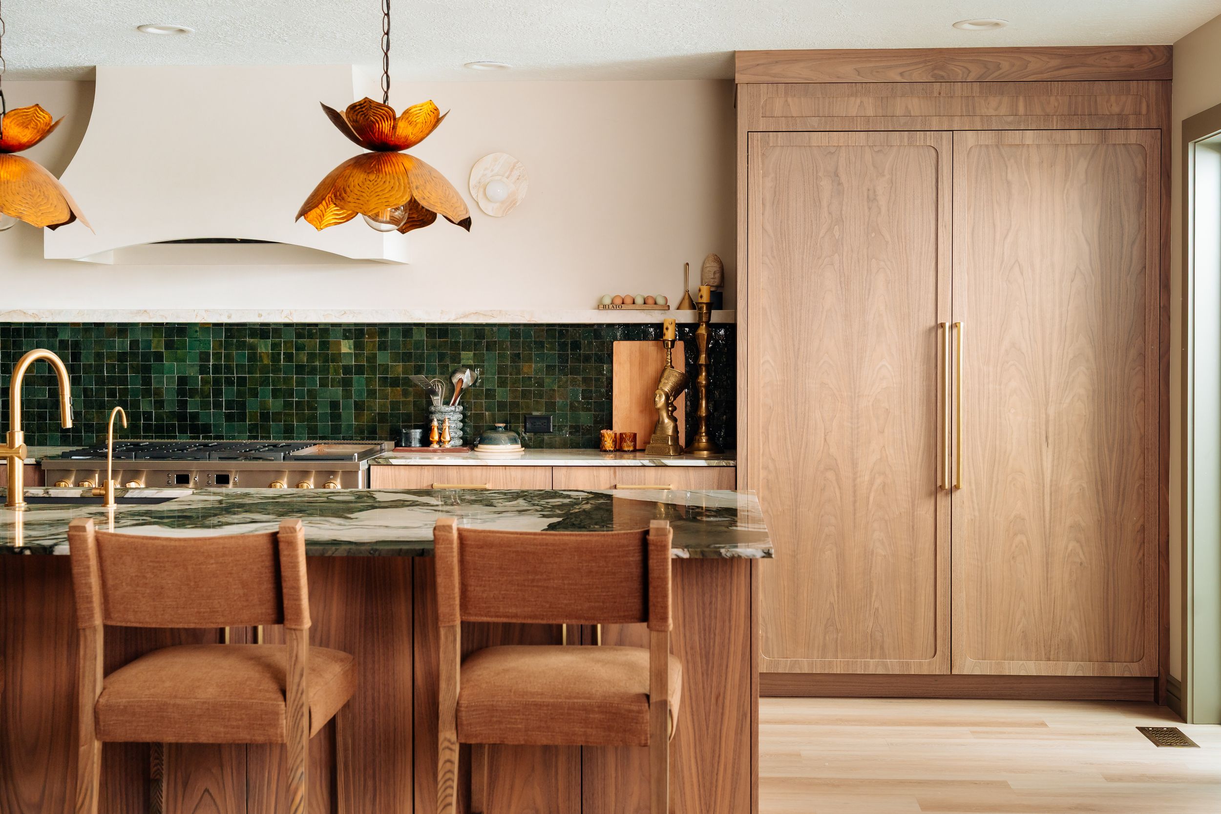Modern kitchen with warm wood cabinets, green mosaic backsplash, brass fixtures, and amber pendant lights over a marble island.