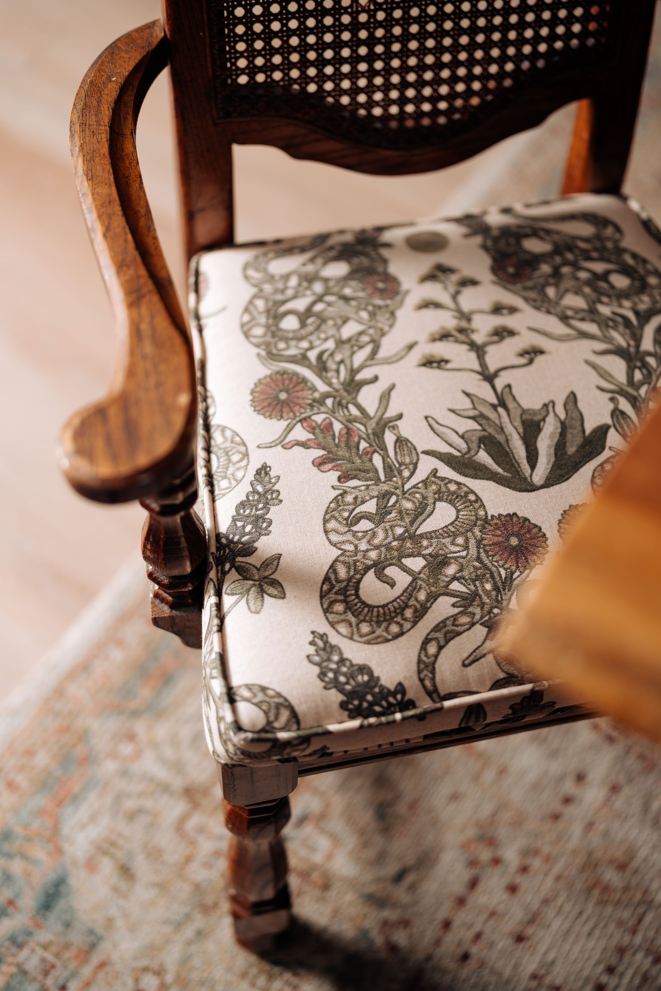 Vintage wooden chair with ornate cane back and botanical snake-print upholstered seat cushion on a patterned rug.