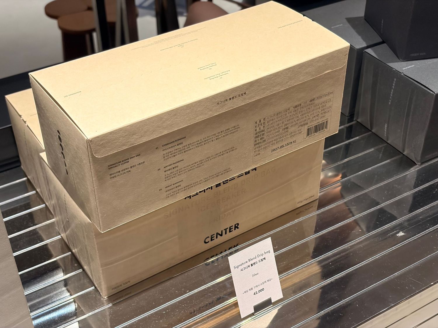 Two sealed cardboard boxes labeled CENTER stacked on a metal shelf in a retail store.