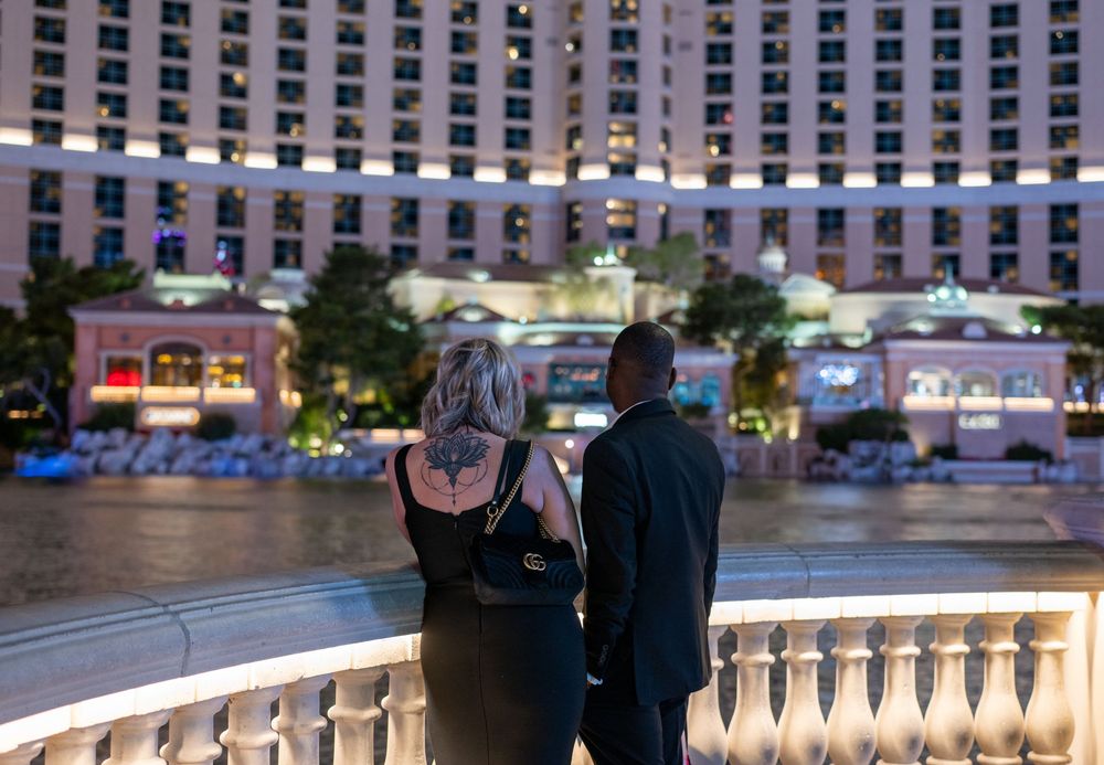 Couple in formal attire standing at Bellagio fountain overlook on the Las Vegas Strip at night.