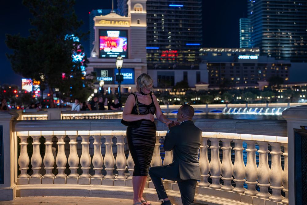 Man proposes to woman on a bridge at night on the Las Vegas Strip with glowing city lights in the background.