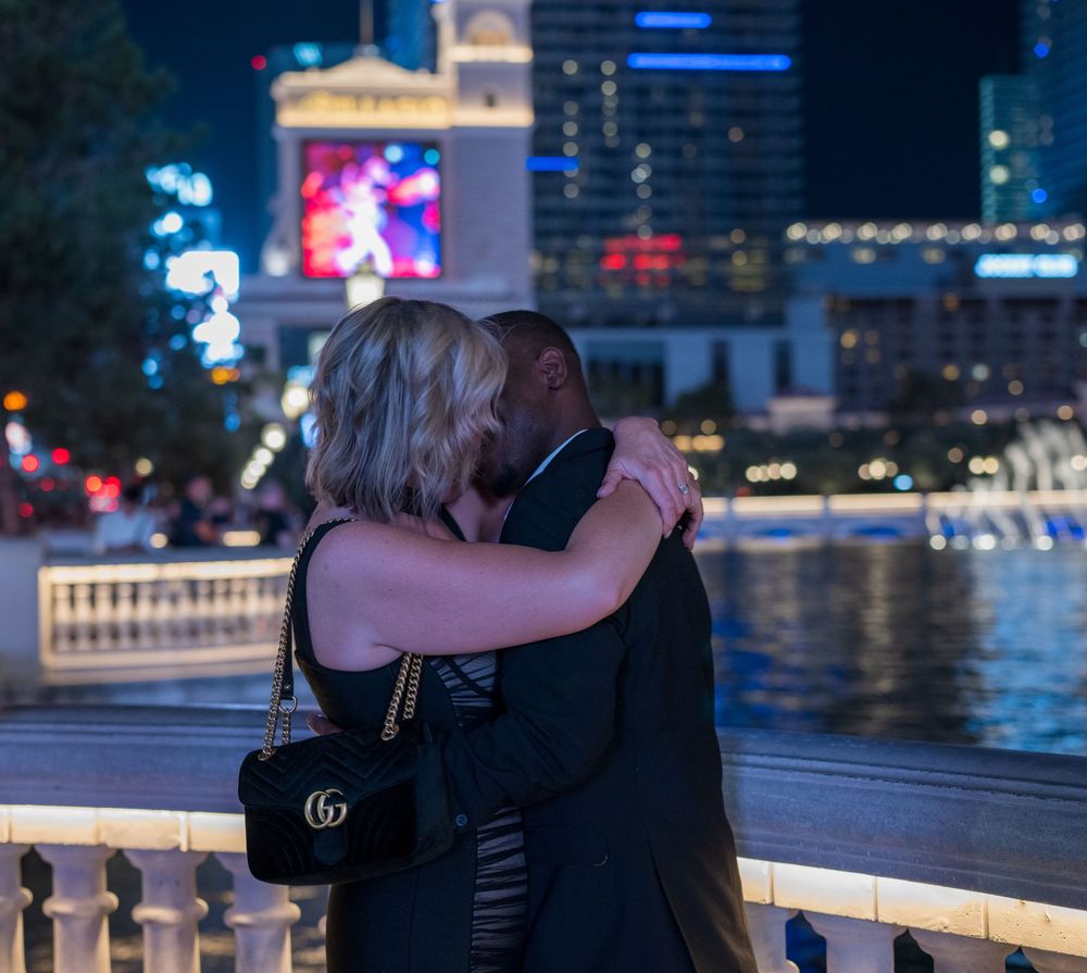 Interracial couple embracing and kissing near Bellagio fountains on Las Vegas Strip at night.