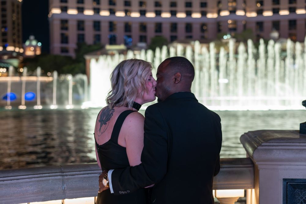 Couple sharing a romantic kiss in front of the illuminated Bellagio fountains at night in Las Vegas.