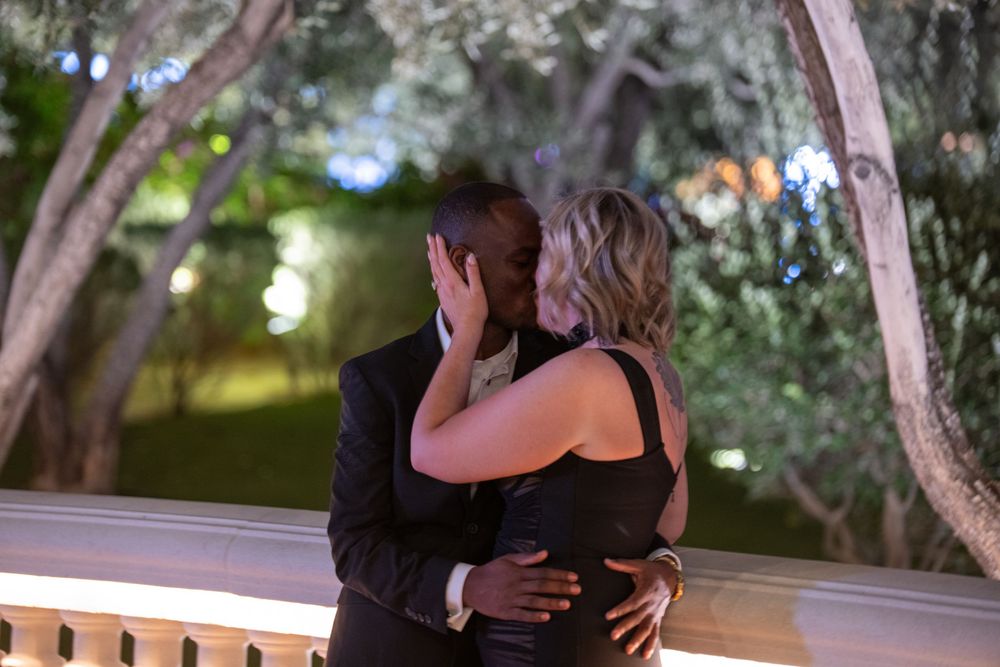 Interracial couple sharing a romantic kiss outdoors at night among trees.