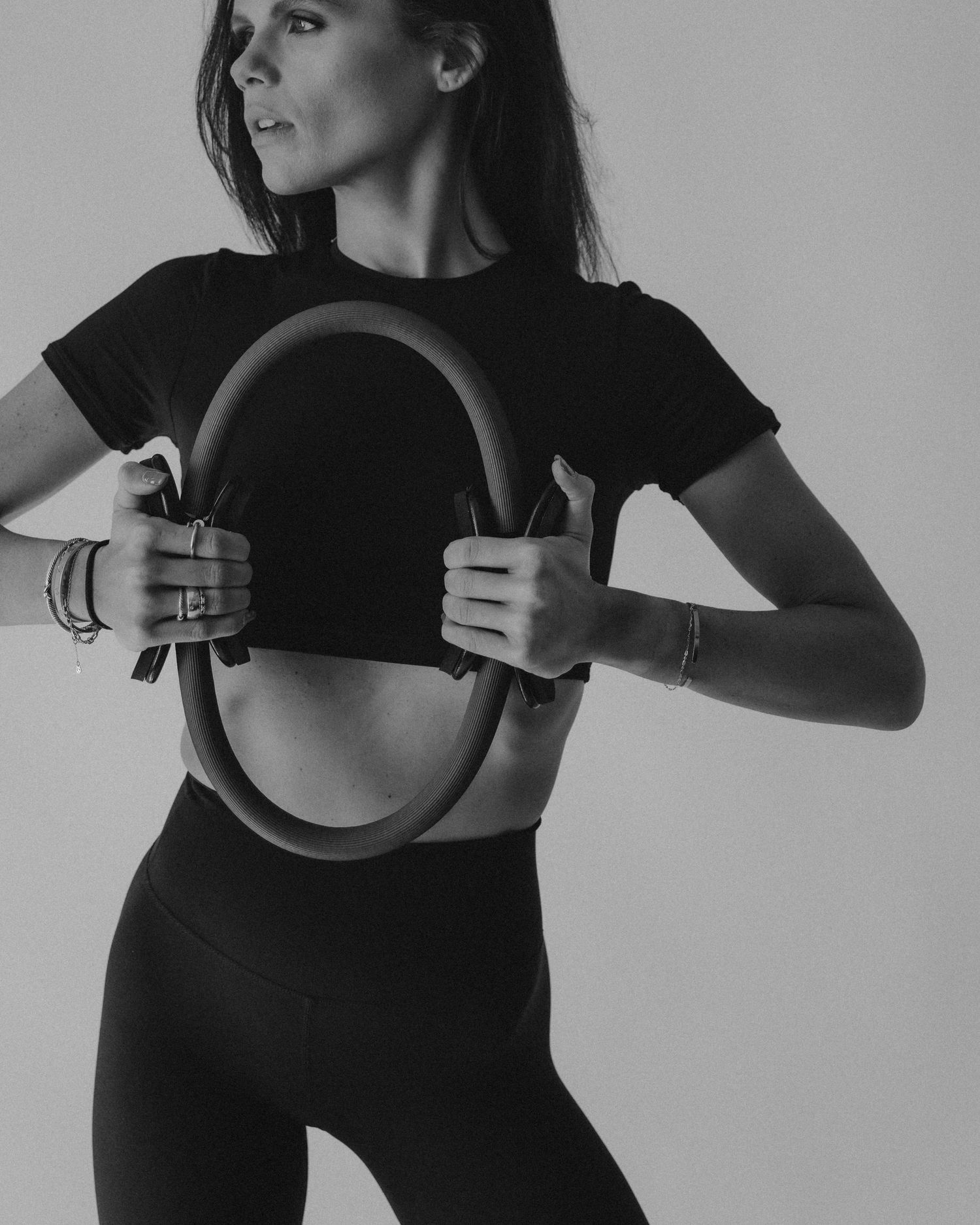 Woman in black crop top and leggings holds a Pilates ring in a black and white fitness photo.