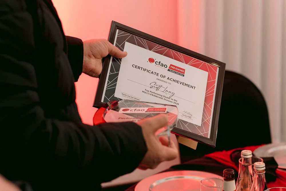Hands holding a CFAO Certificate of Achievement at a formal awards ceremony with red decor.