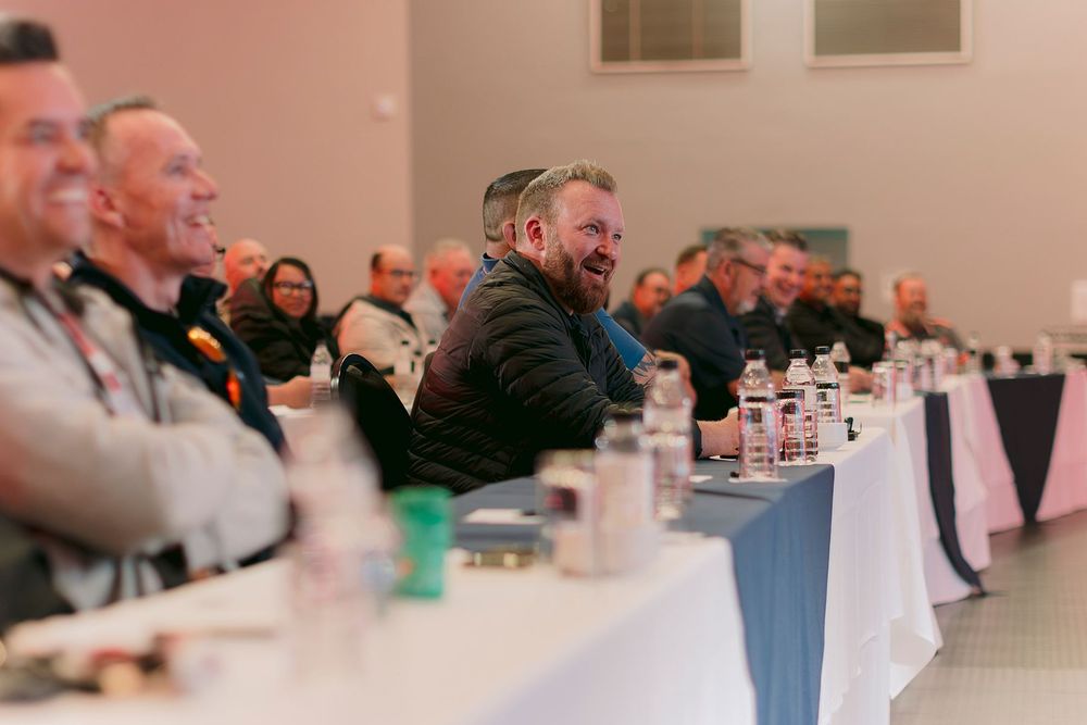 Group of men laughing and smiling while seated at a long banquet table during a formal conference event.