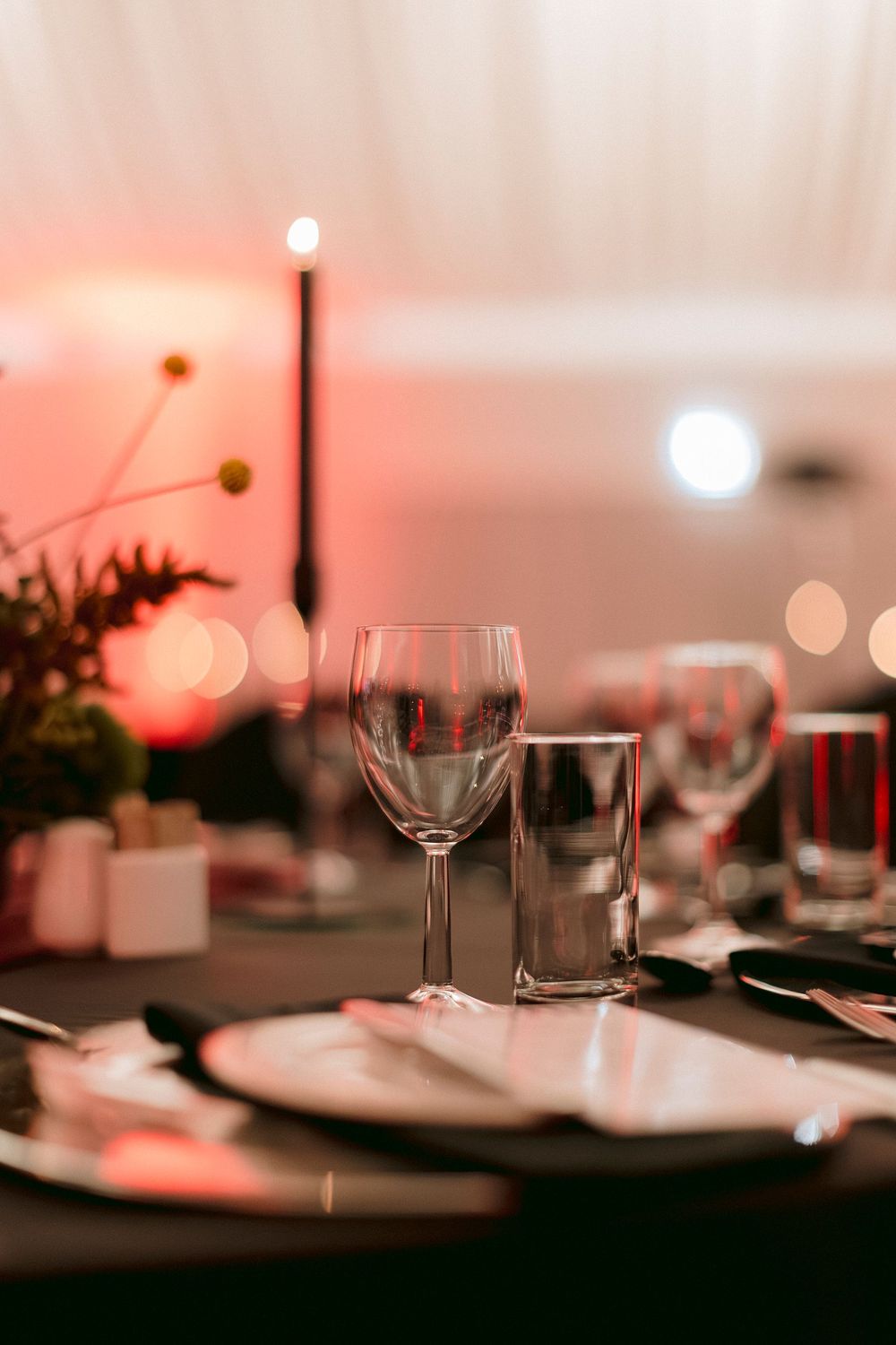 Elegant wedding reception table setting with crystal wine glasses, candles, and soft pink ambient lighting.
