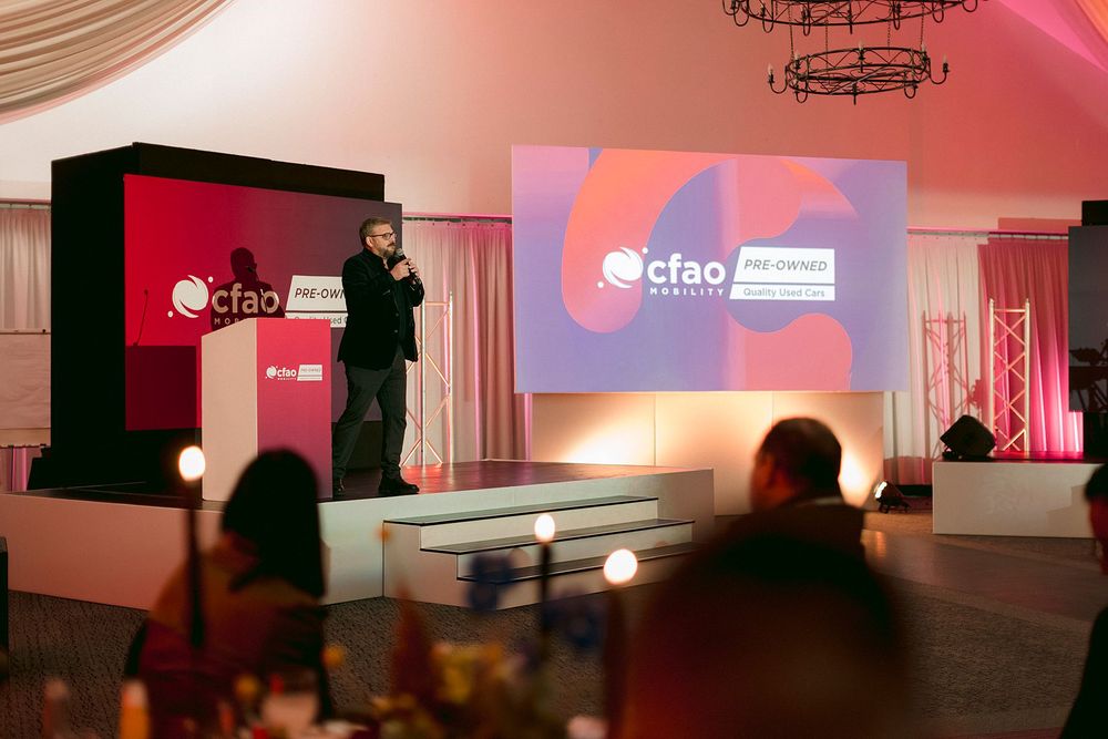 A speaker presents on stage at a CFAO corporate event in an elegantly decorated venue with pink lighting.