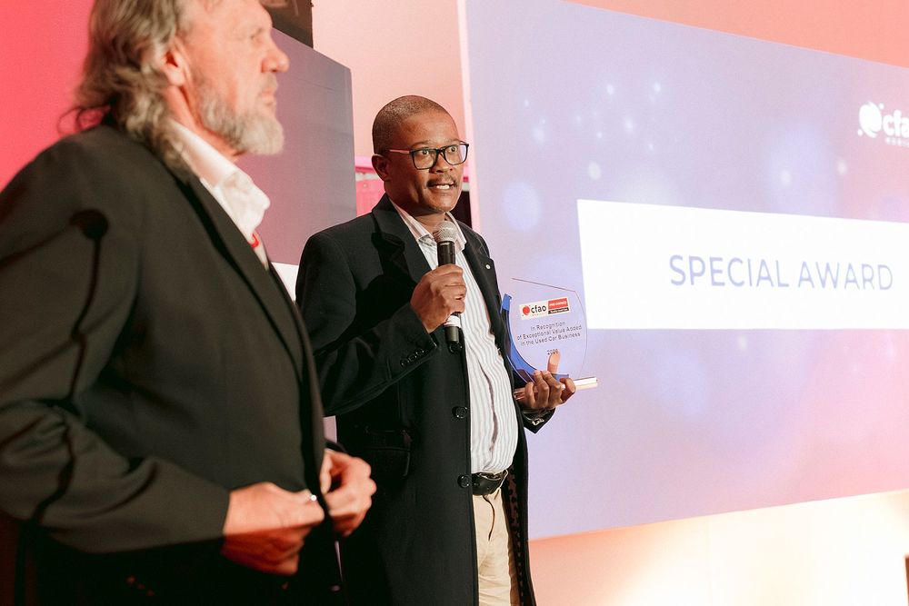 Two men on stage at a Special Award ceremony, one holding a microphone and award trophy under event lighting.