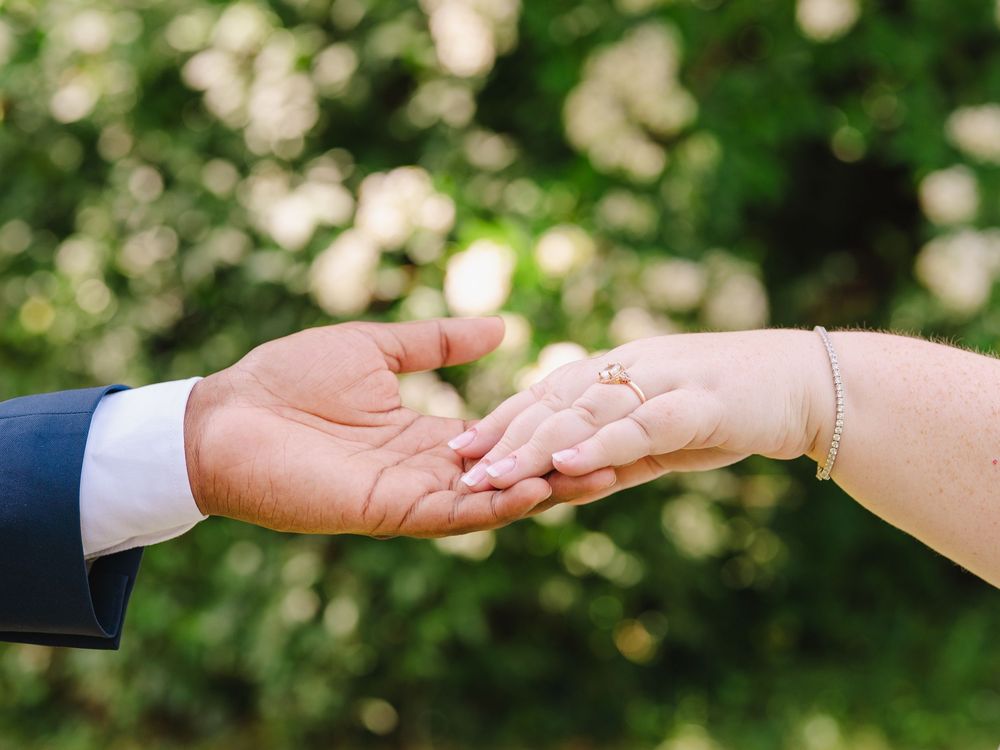 Close-up view of two hands reaching towards each other with blurred green foliage and white flowers in the background.