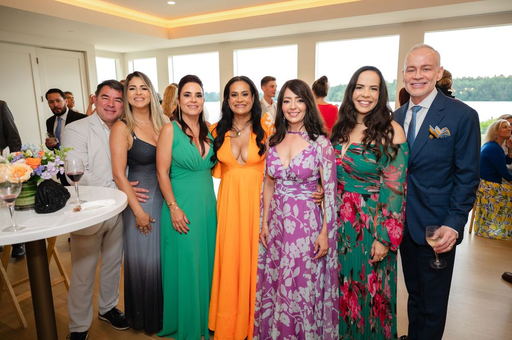 A group of party guests in colorful formal attire pose together at an elegant reception venue with warm lighting.