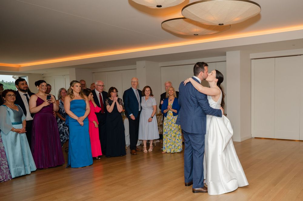 Wedding guests dance and celebrate in an elegant banquet hall with warm overhead lighting and a hardwood dance floor.
