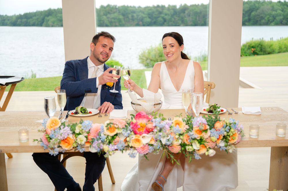 A bride and groom cheers at the sweetheart table during a wedding reception at the Lakehouse in Halifax, MA