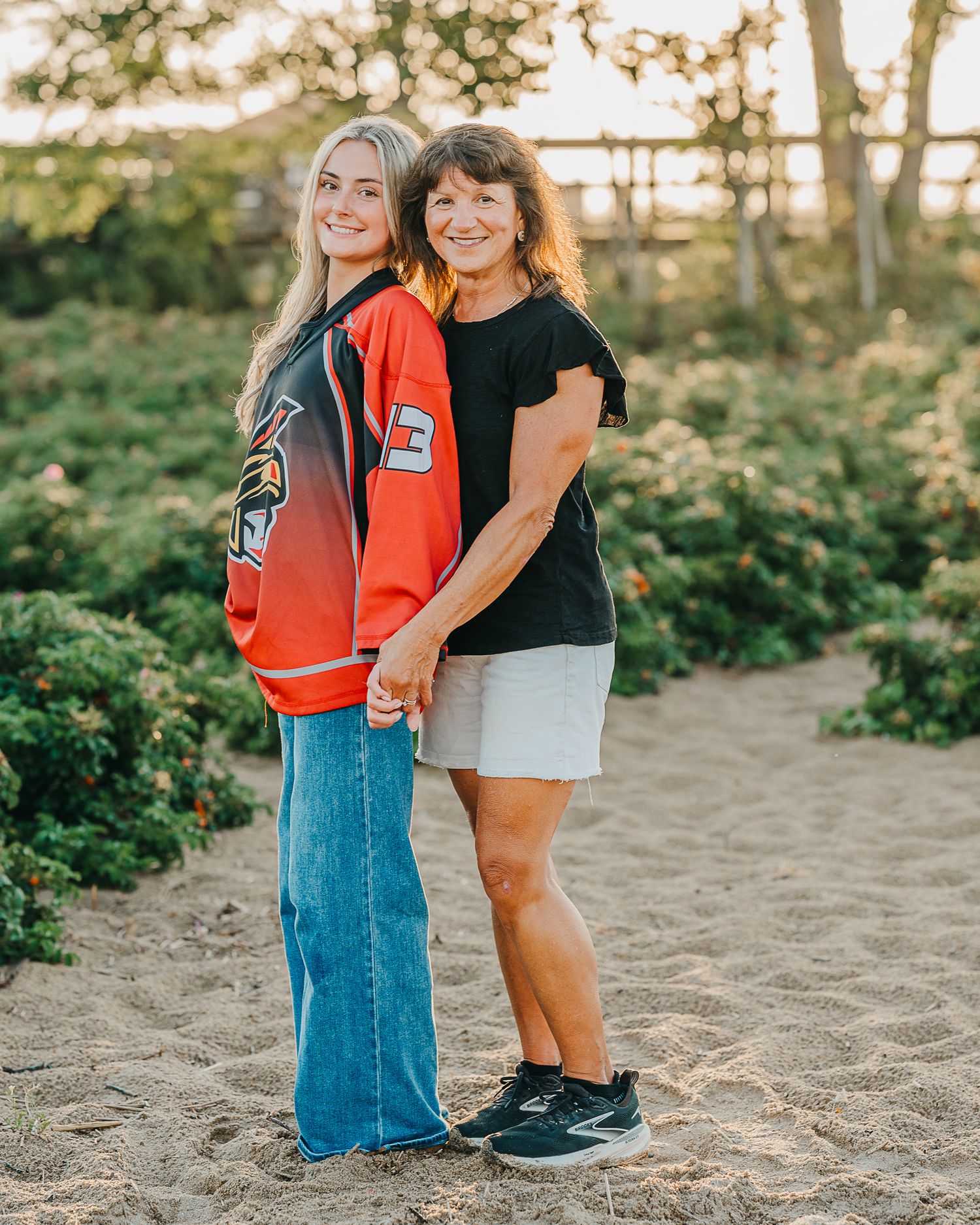 A mother and daughter share a warm embrace while standing on sandy ground during senior girls golden hour photoshoot