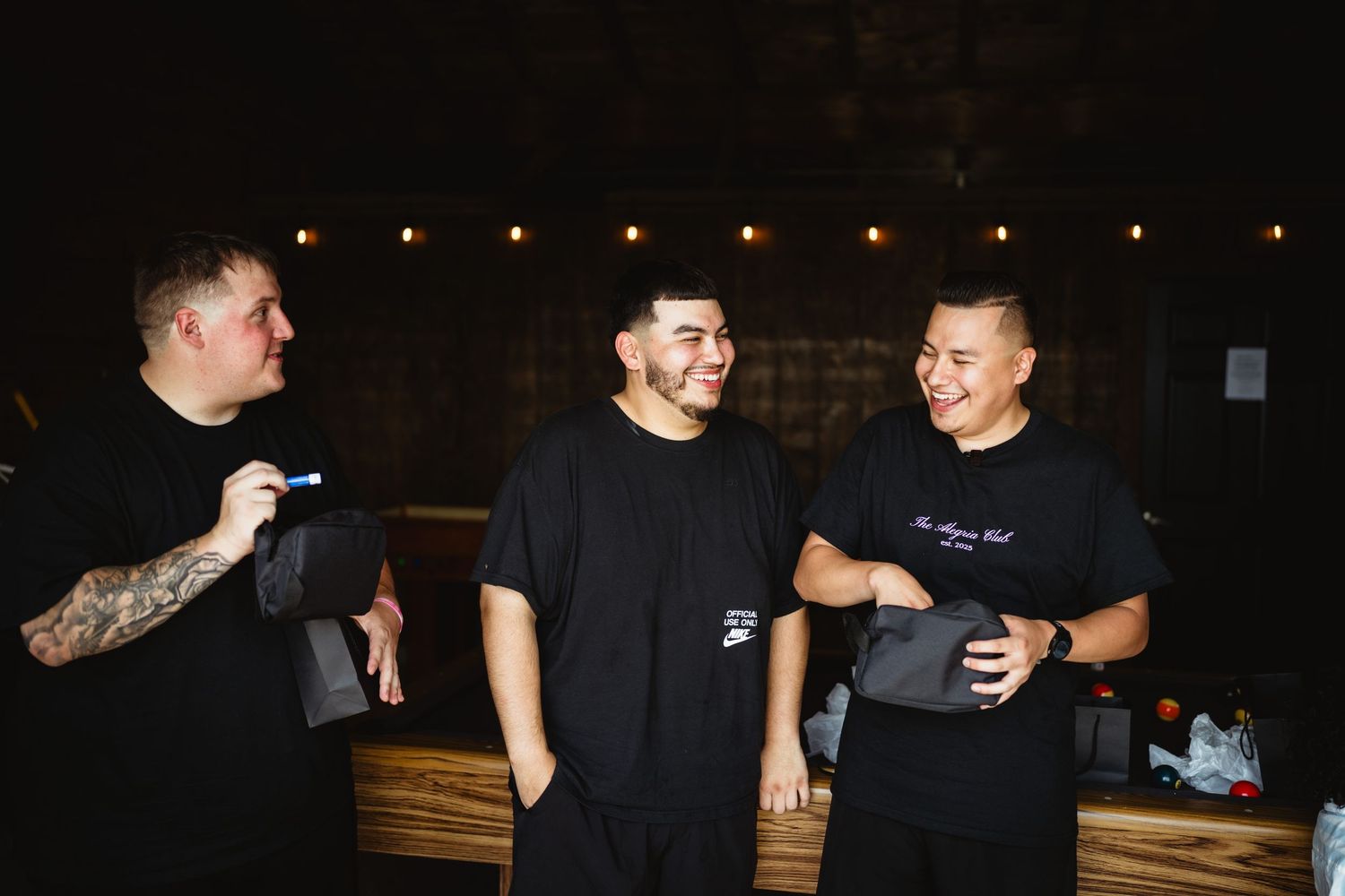Three people standing together having a conversation and laughing at a dimly lit venue at night.