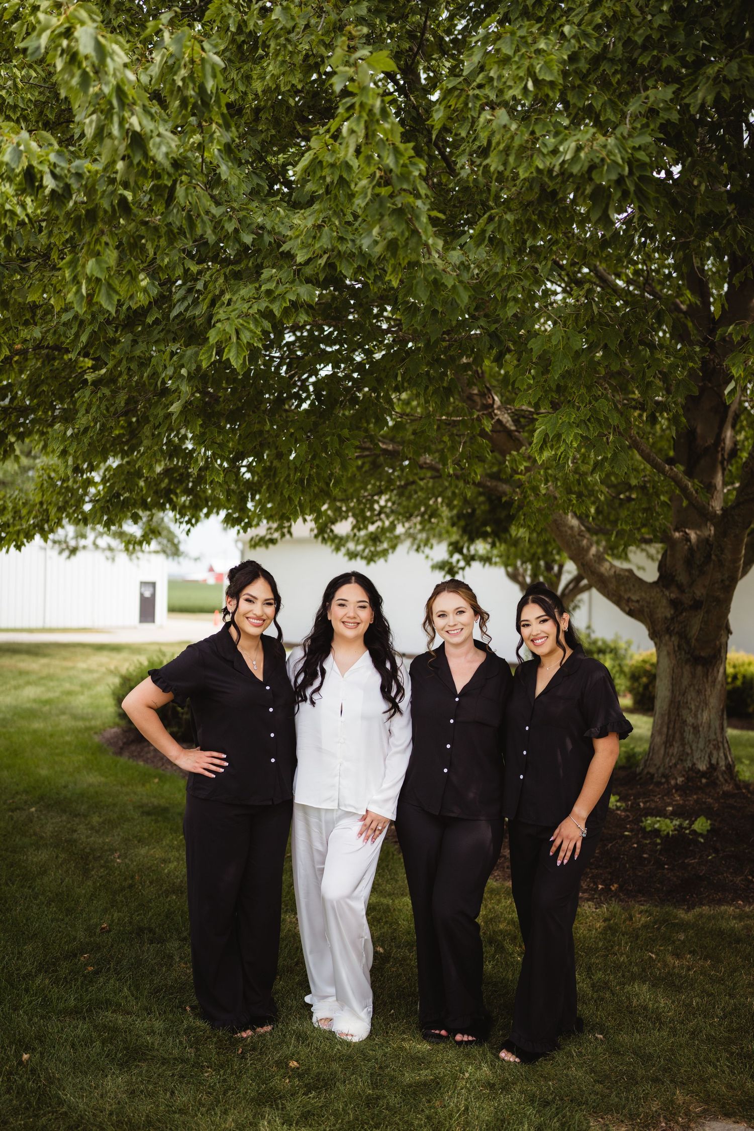 Four people stand together under a leafy green tree wearing coordinated black and white outfits.