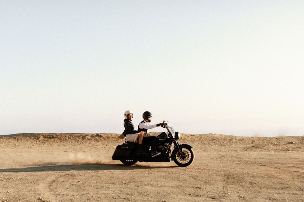 Couple riding a motorcycle together through a sandy desert landscape at dusk.