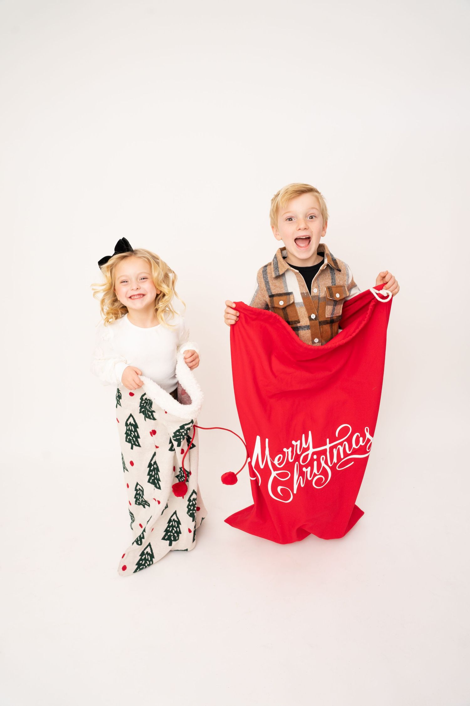 Children display festive Christmas decorations and signs in white studio setting.