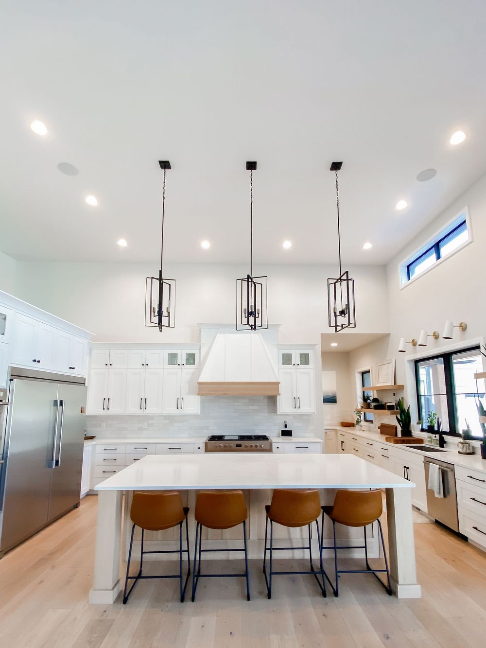 Contemporary white kitchen with leather bar stools and pendant lighting over large island.