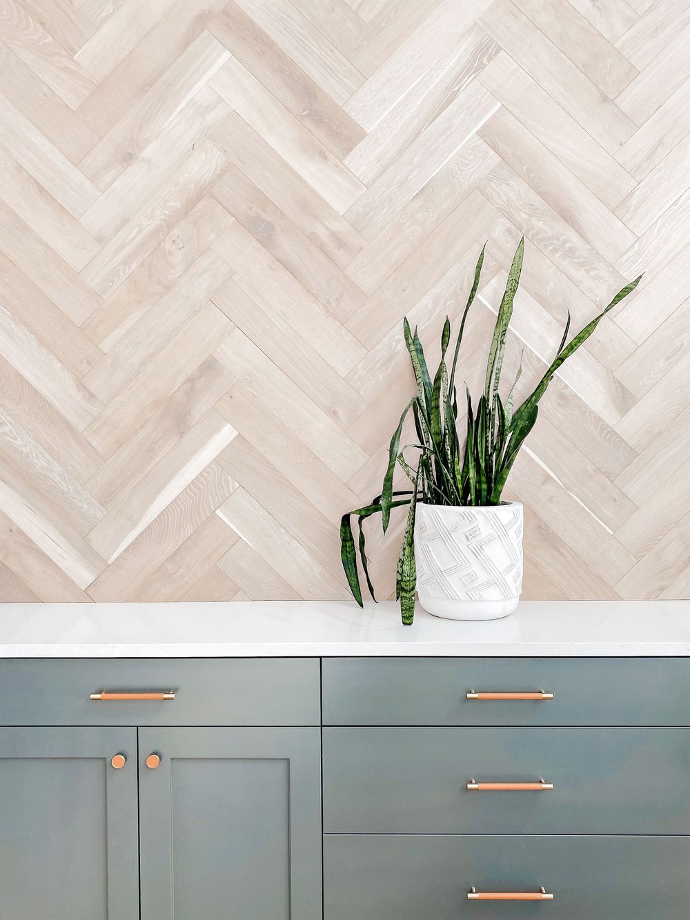 Minimalist interior featuring herringbone wood floors and sage green cabinets with copper handles.