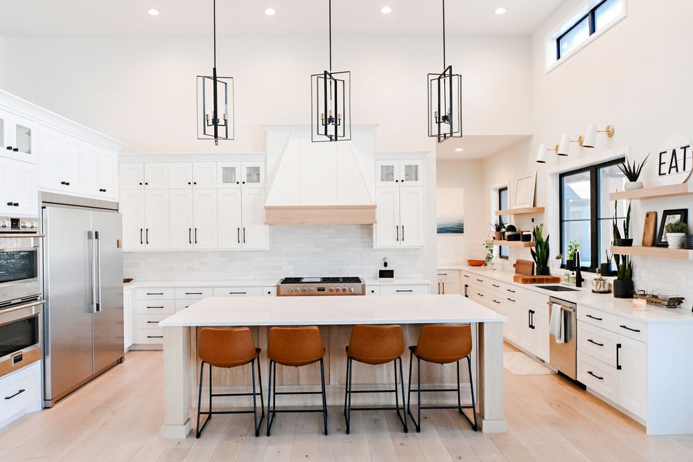 Modern white kitchen with pendant lights and leather bar stools along a large island counter.