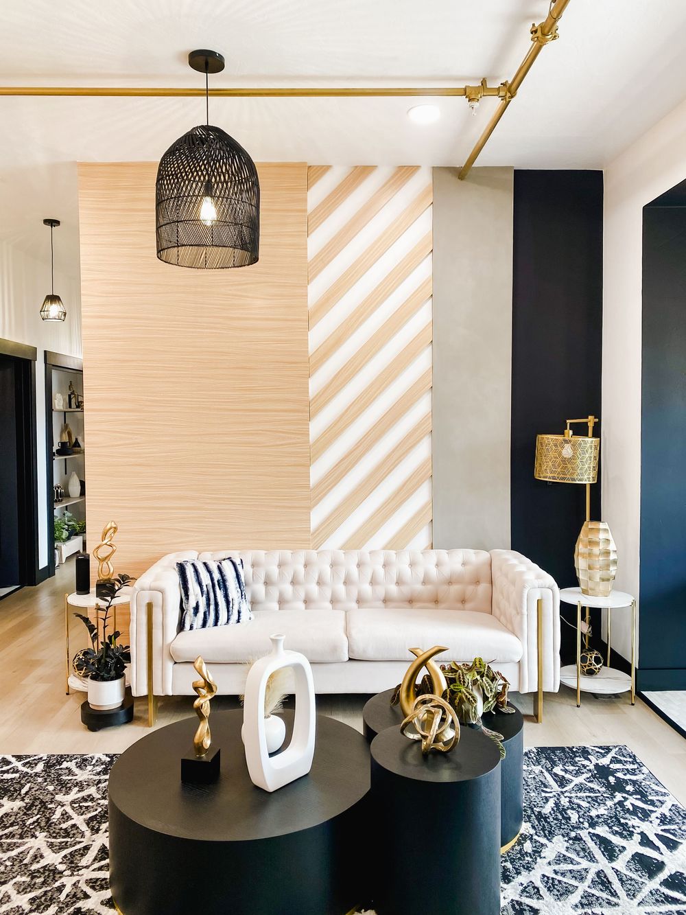 Modern living room with tufted white couch, black accent wall, and gold decorative elements on round side tables.